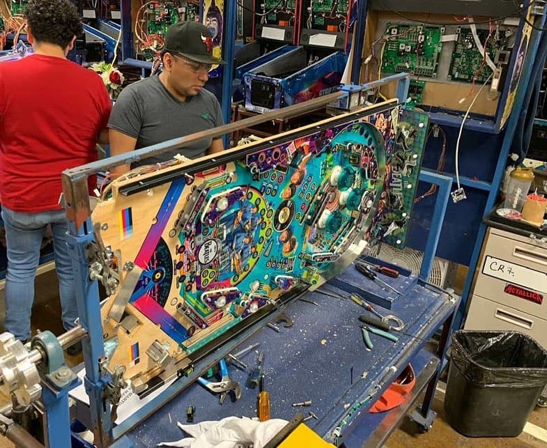 Technician repairing colorful pinball machine in workshop with circuit boards