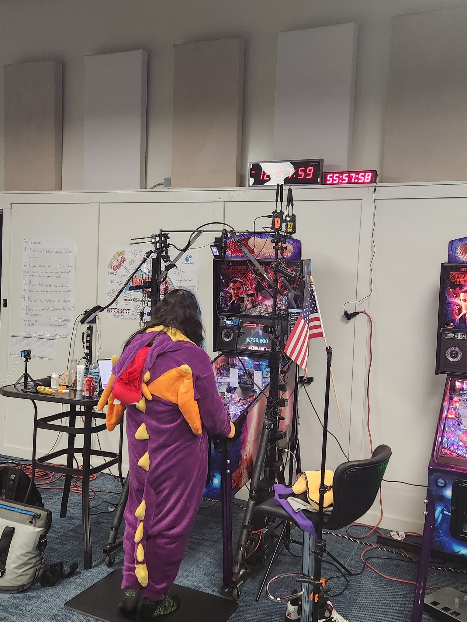 Dinosaur-costumed person playing pinball machine with Stranger Things backdrop