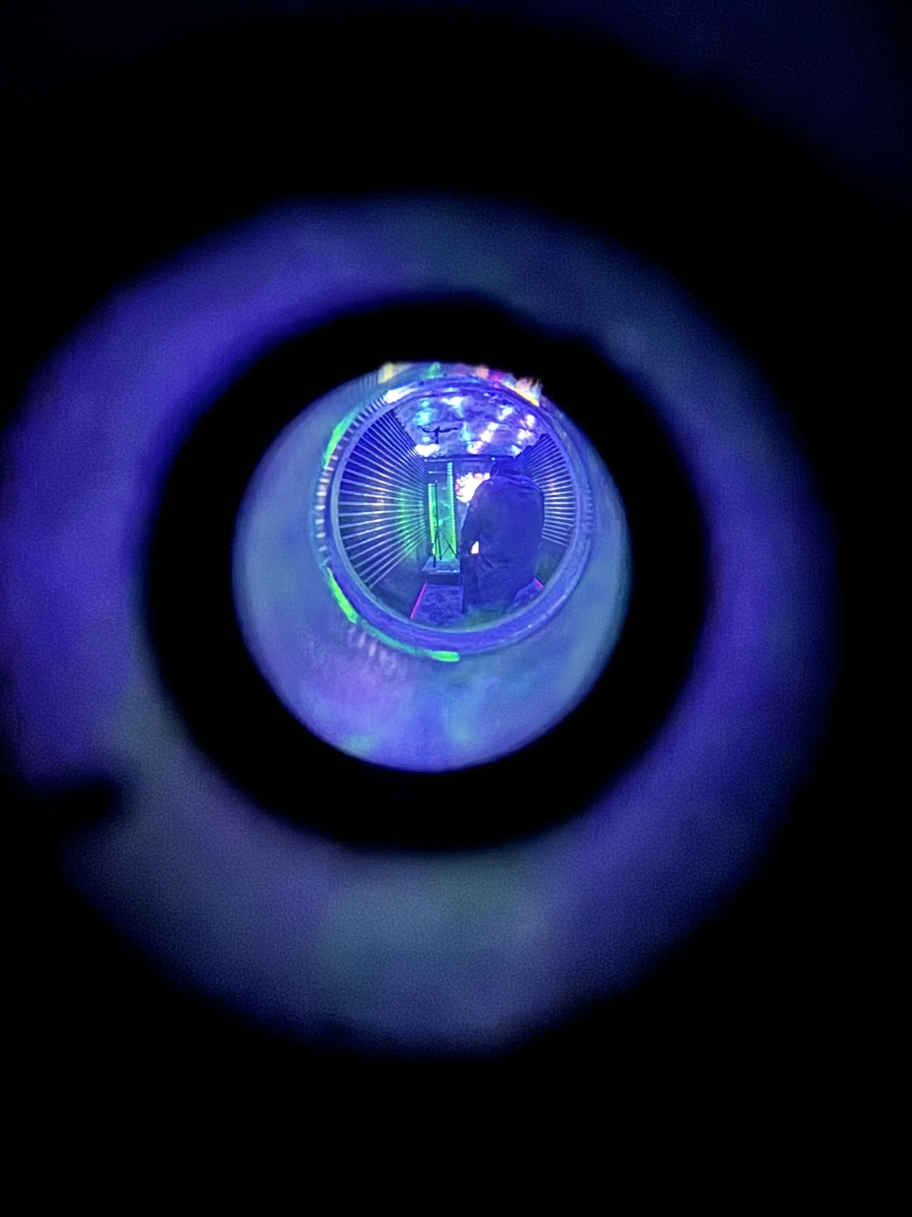 Blue and green glowing orb with radial pattern viewed through circular lens