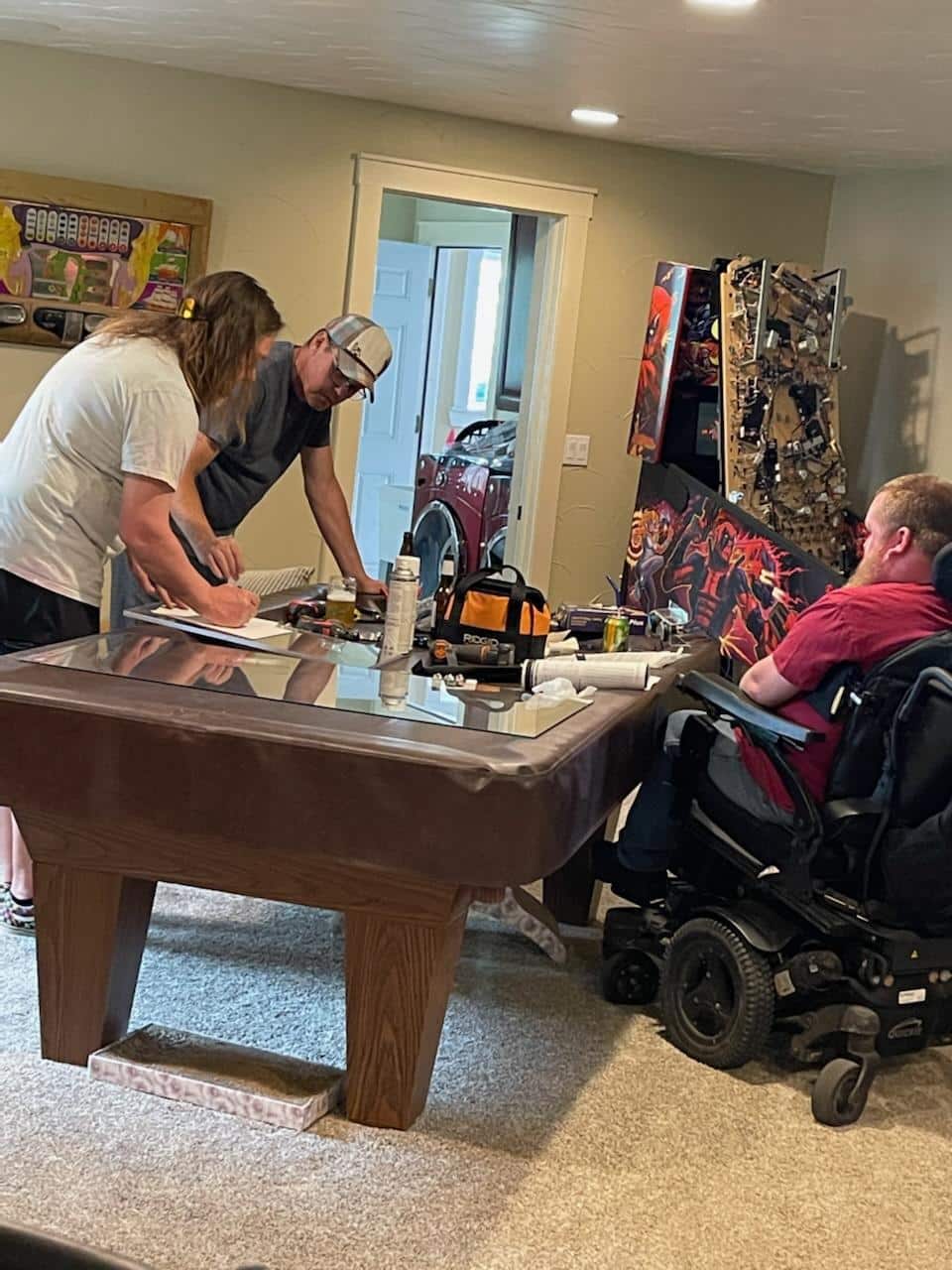 Two people working together at a table while person in wheelchair observes