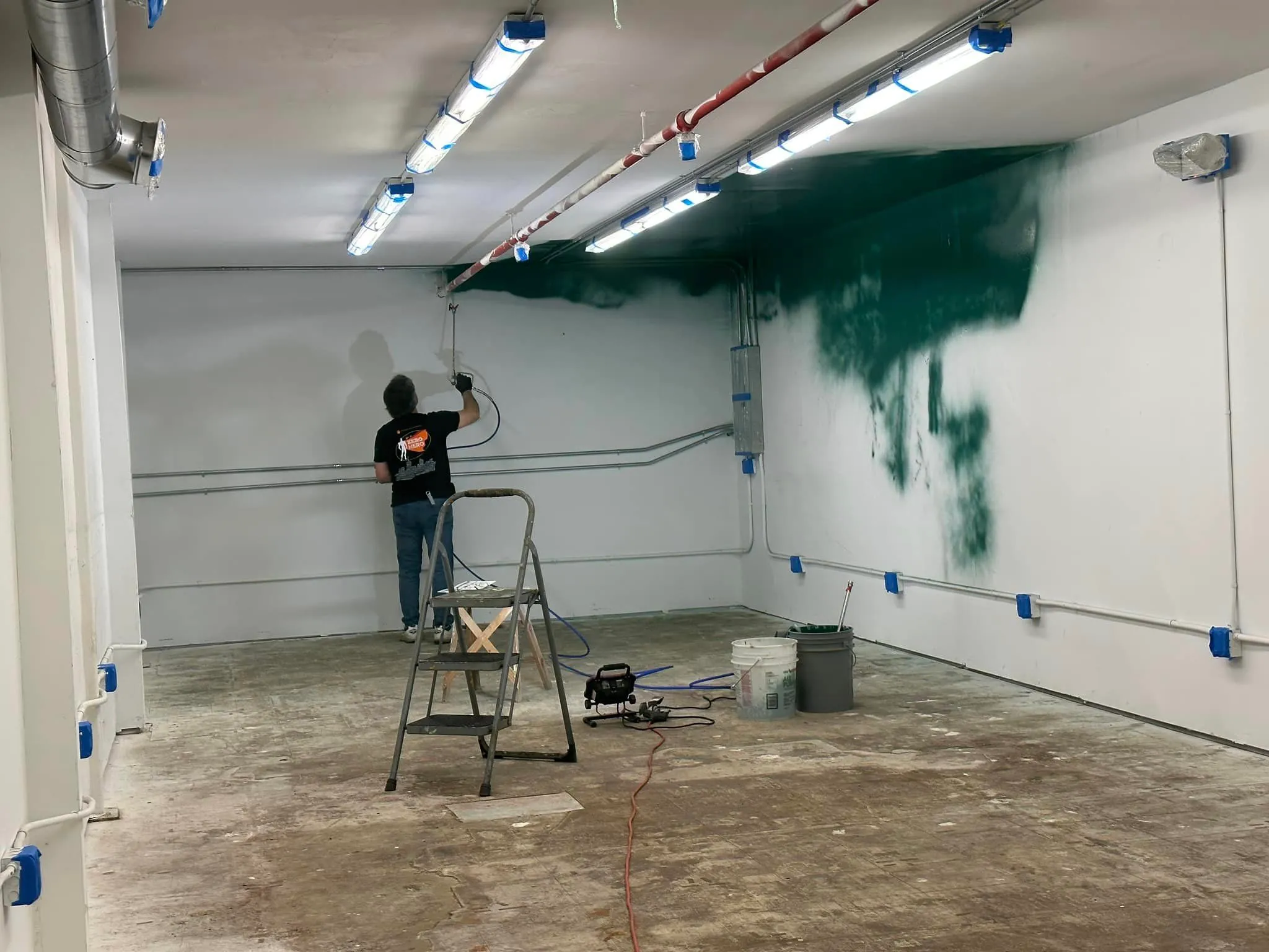 Person spray painting green mist on wall in industrial workspace