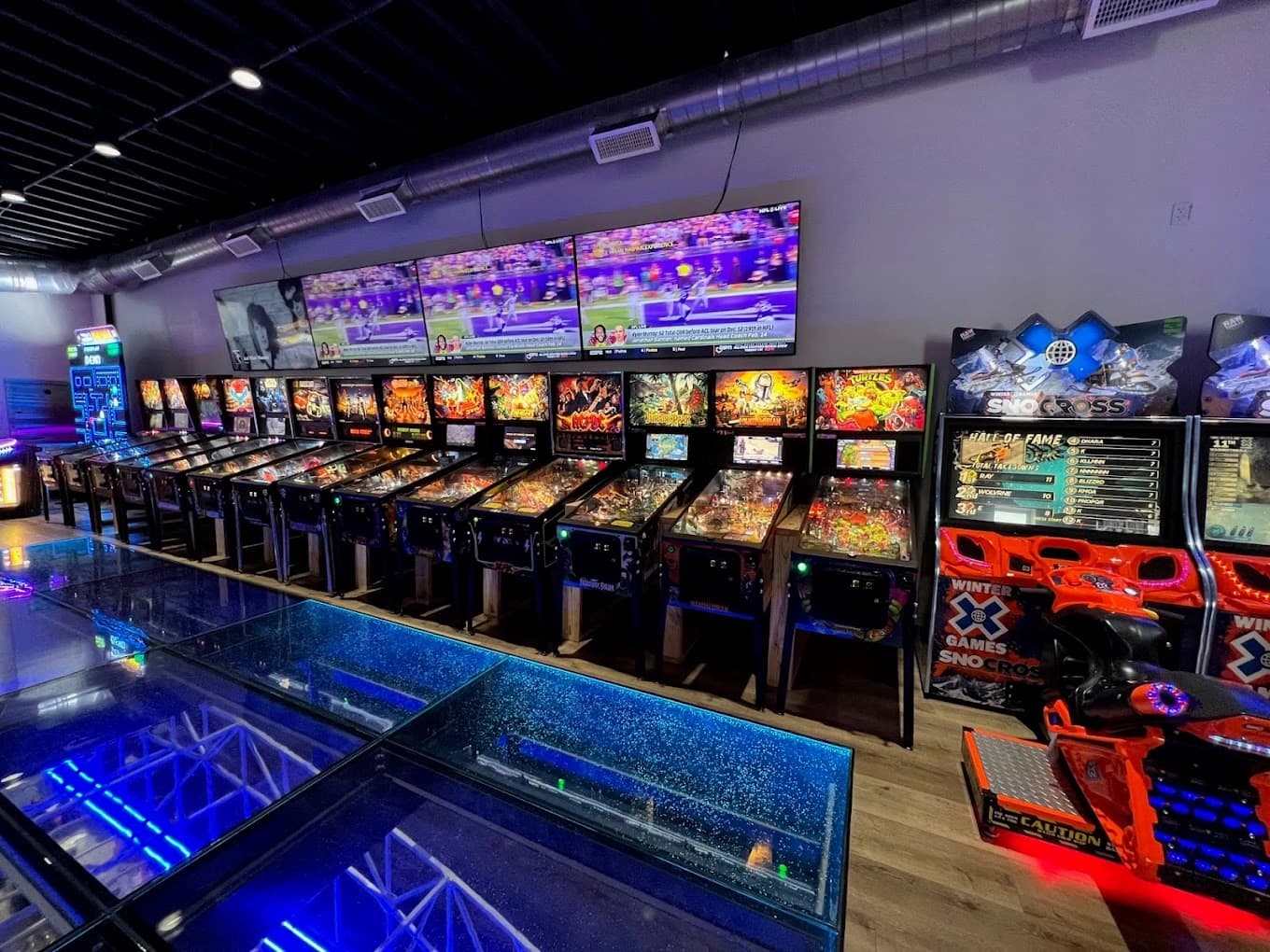 Colorful arcade with multiple pinball machines and sports screens