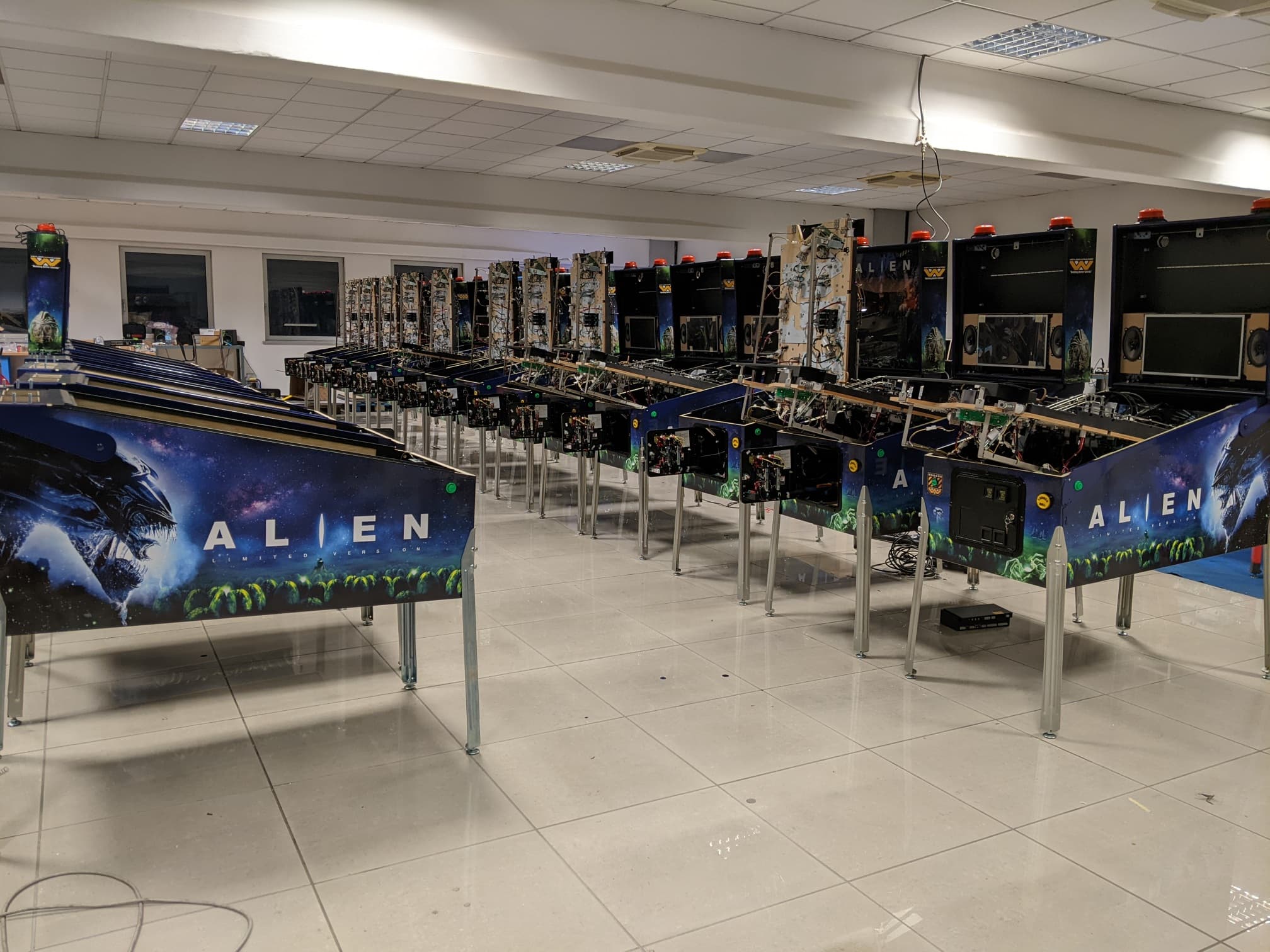Alien-themed pinball machines lined up in a clean, bright workshop