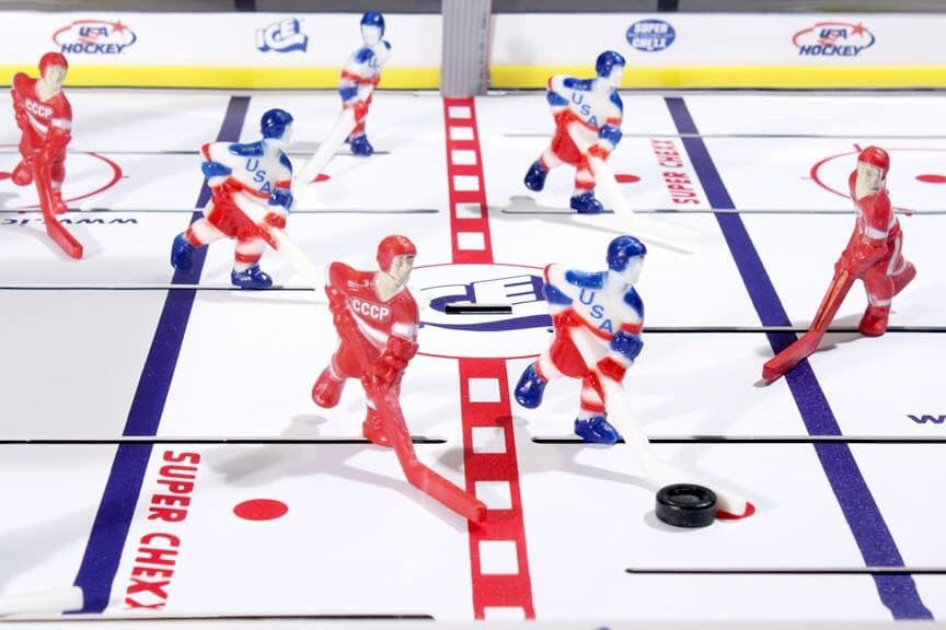 Tabletop hockey game with red and blue players positioned on ice rink