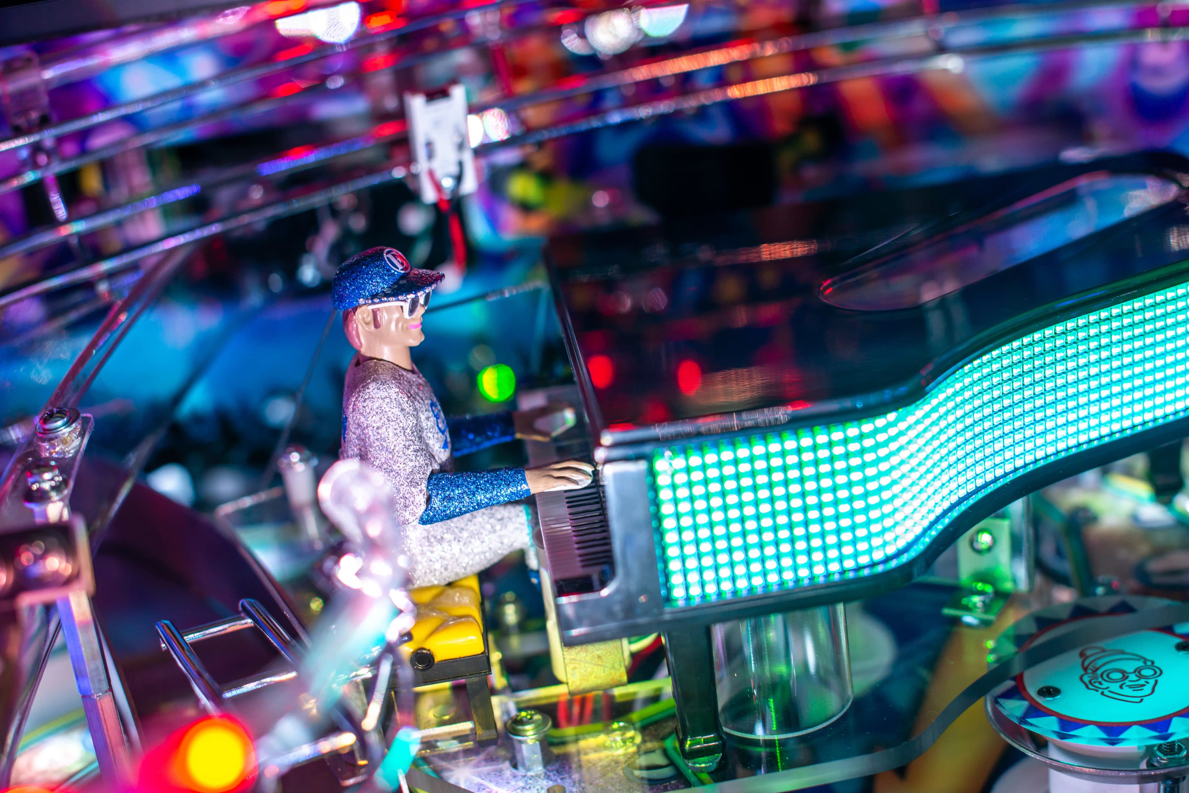 Colorful pinball machine with glowing LED display and small figurine player