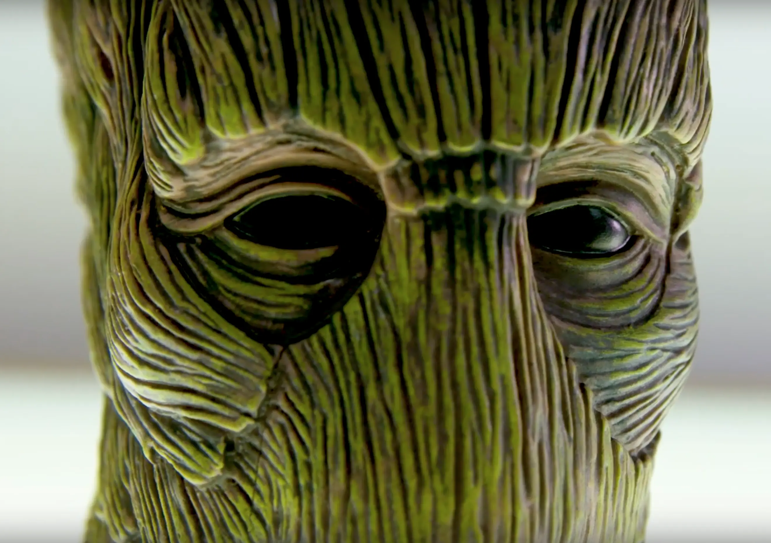 Textured green alien-like face with intricate wood-grain-like patterns