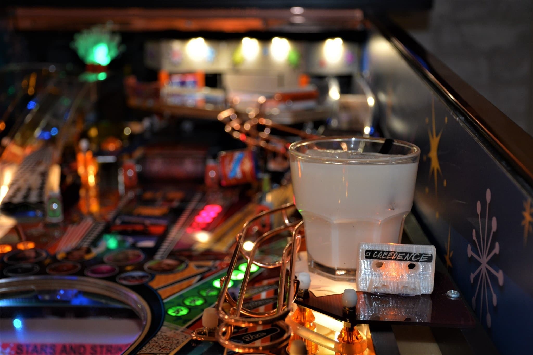 Pinball machine with colorful lights, drink, and Creedence cassette tape