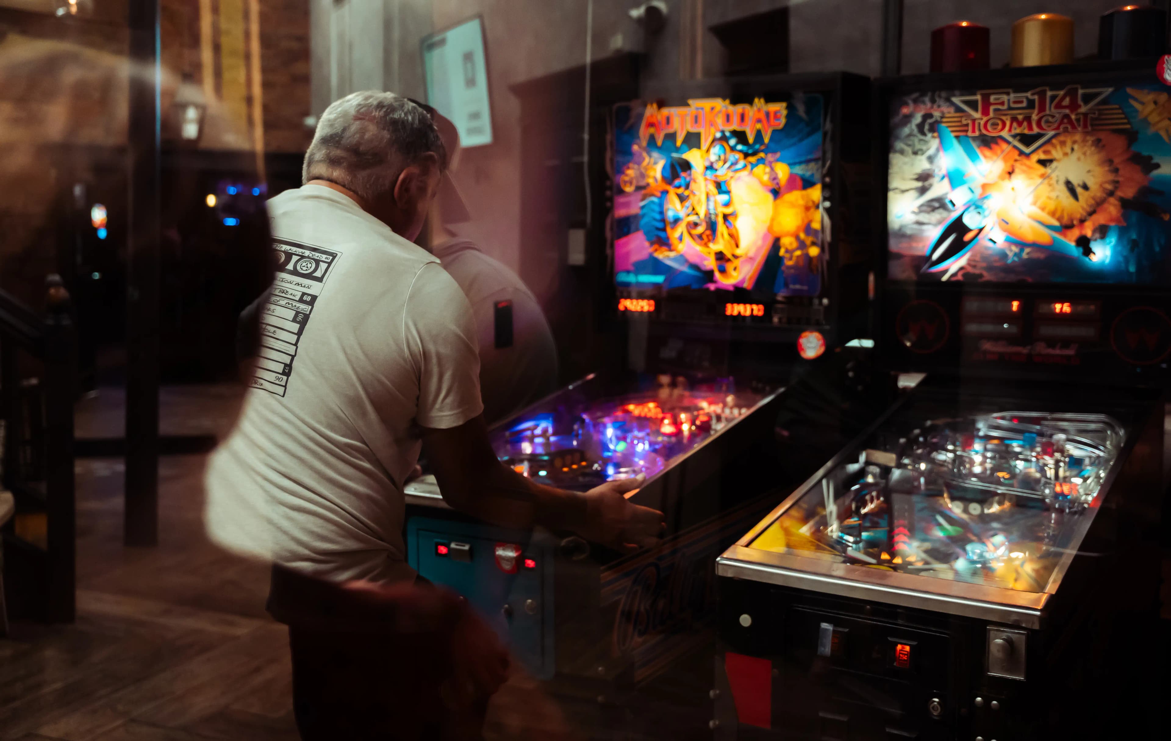 Person playing colorful pinball machines in dimly lit arcade