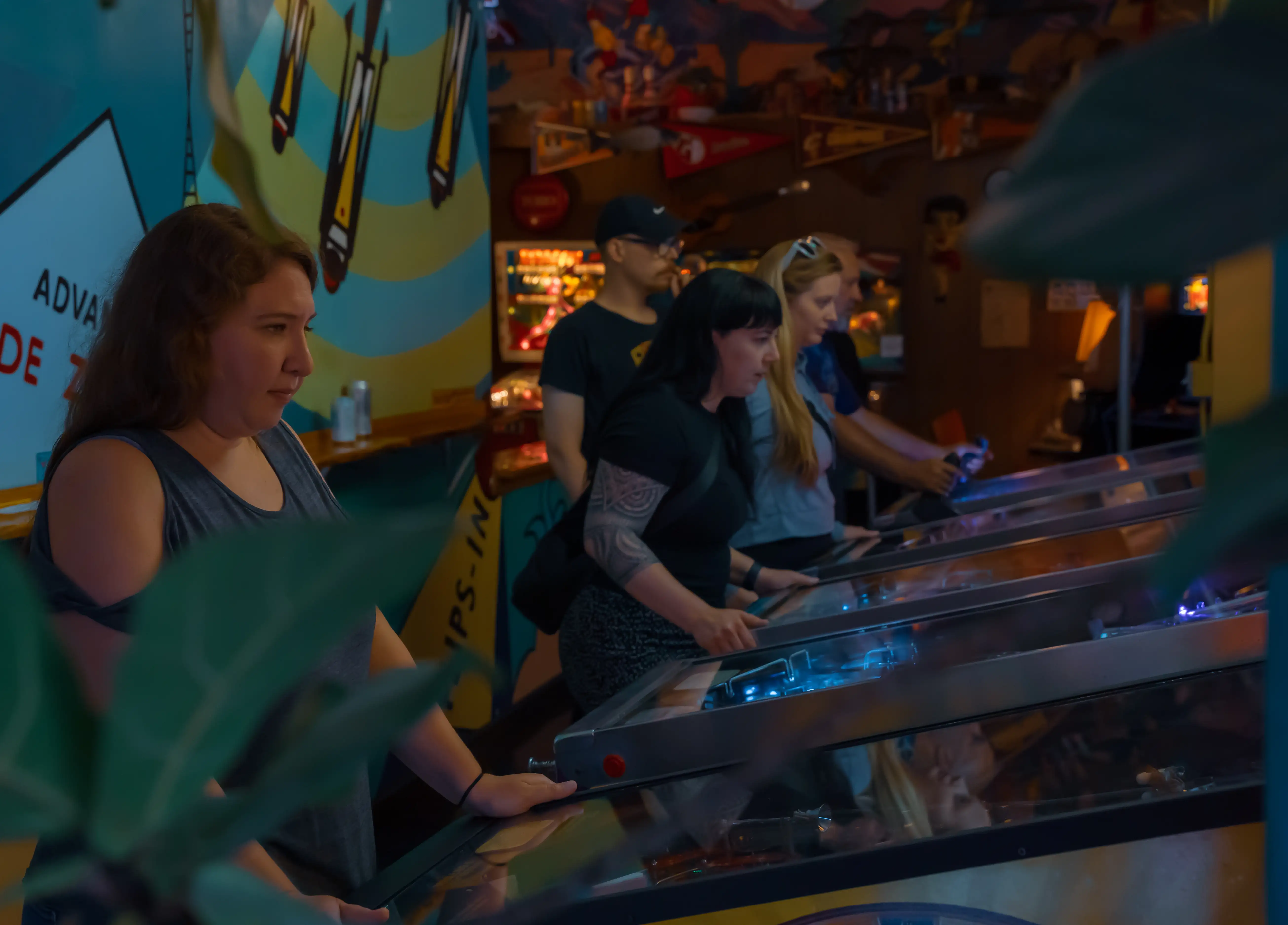 People playing pinball machines in a dimly lit arcade