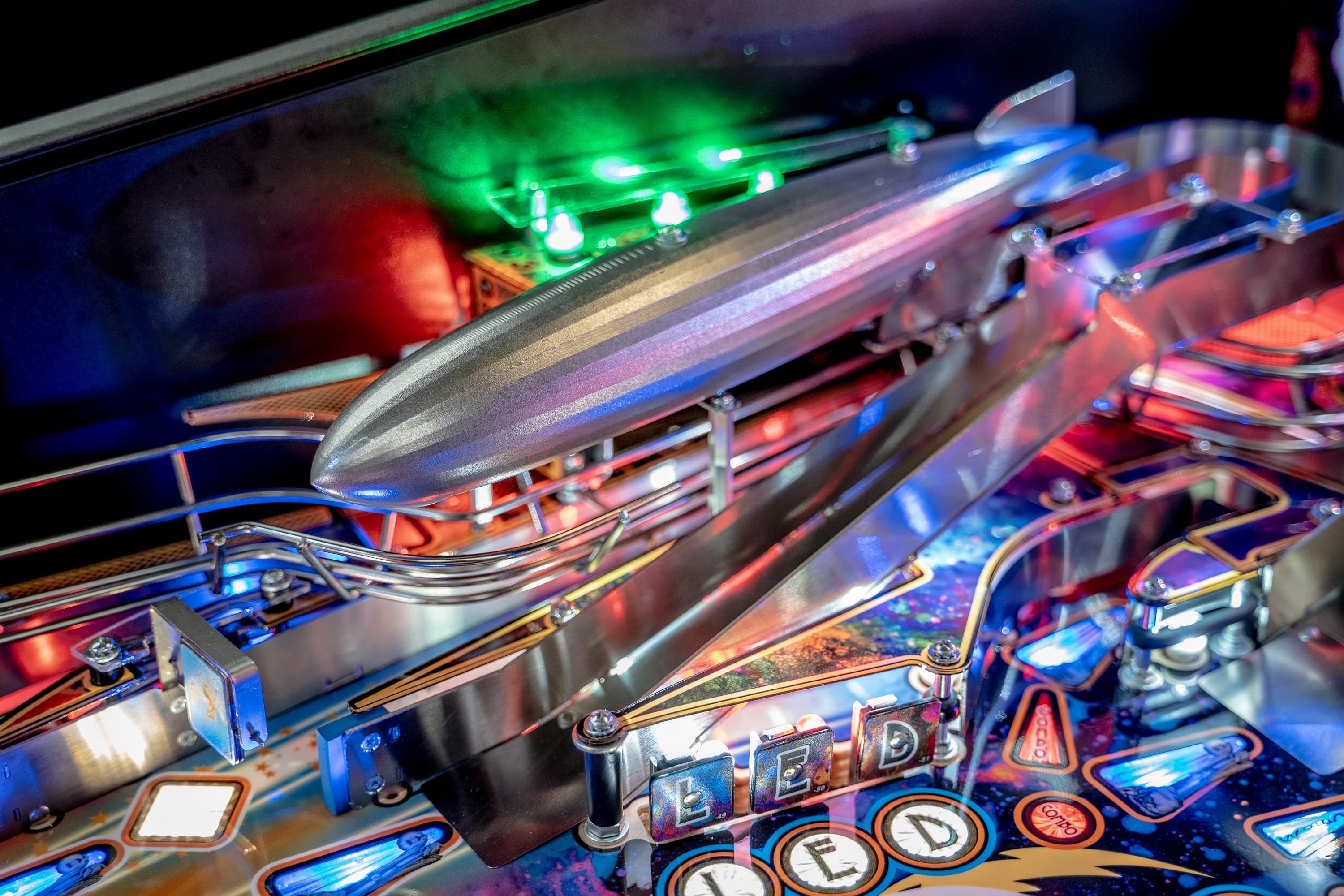 Colorful pinball machine with silver spaceship and vibrant green lights