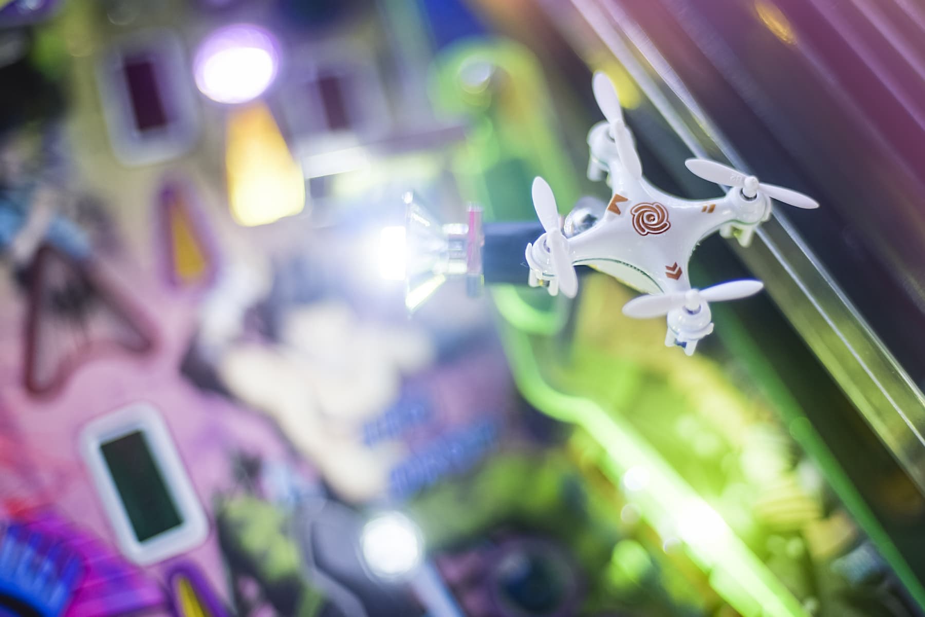 Small white drone hovering amid colorful blurred electronic devices and lights