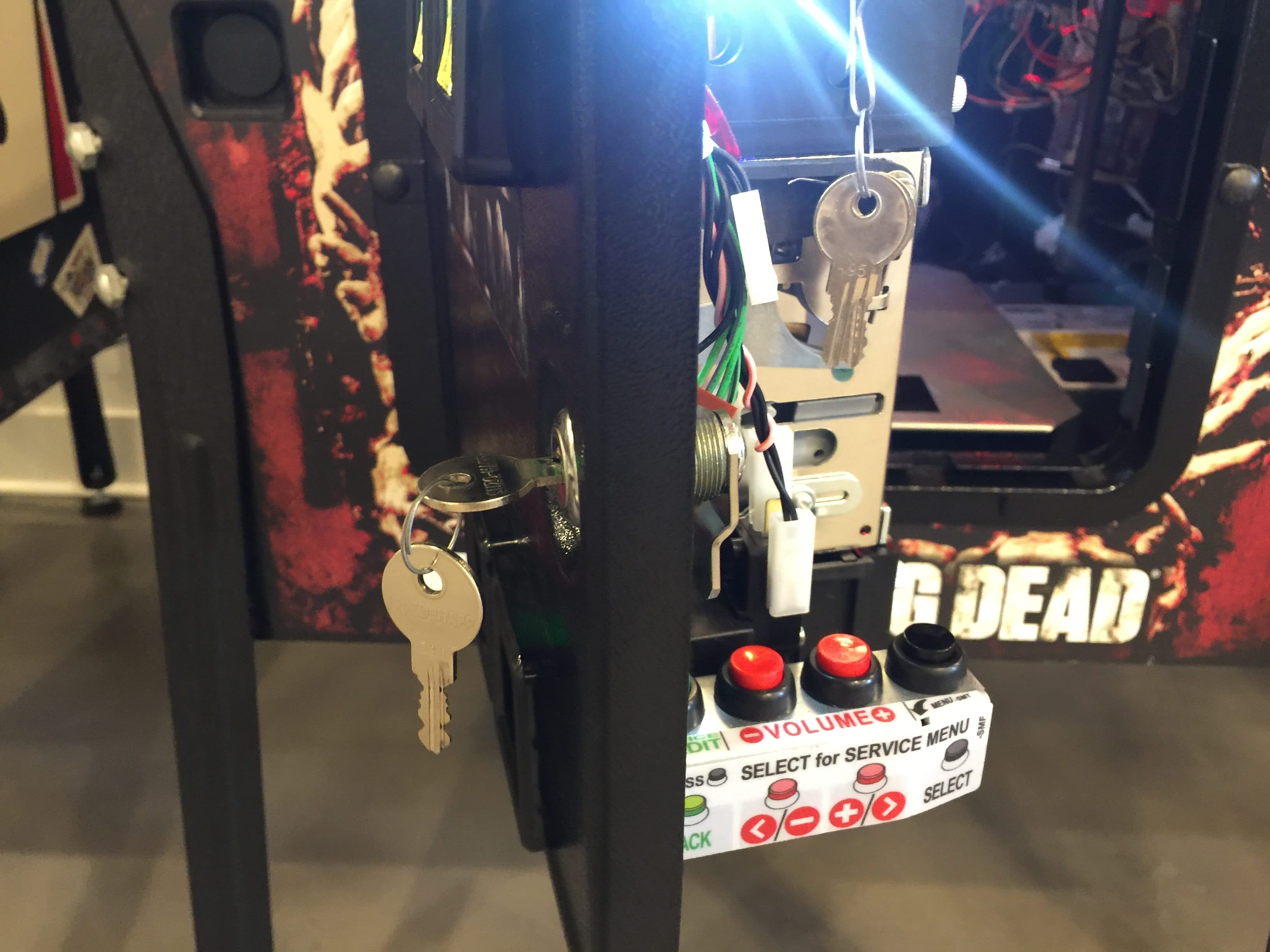 Arcade machine control panel with keys, red buttons, and Walking Dead poster