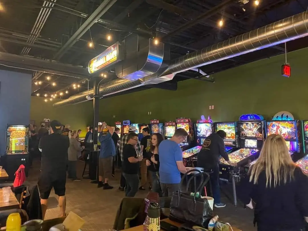 Crowded pinball arcade with colorful machines and string lights