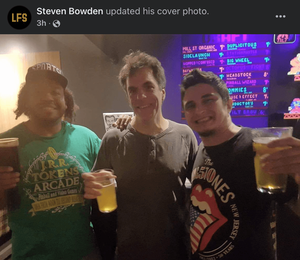 Three friends enjoying beers in front of a colorful craft beer menu