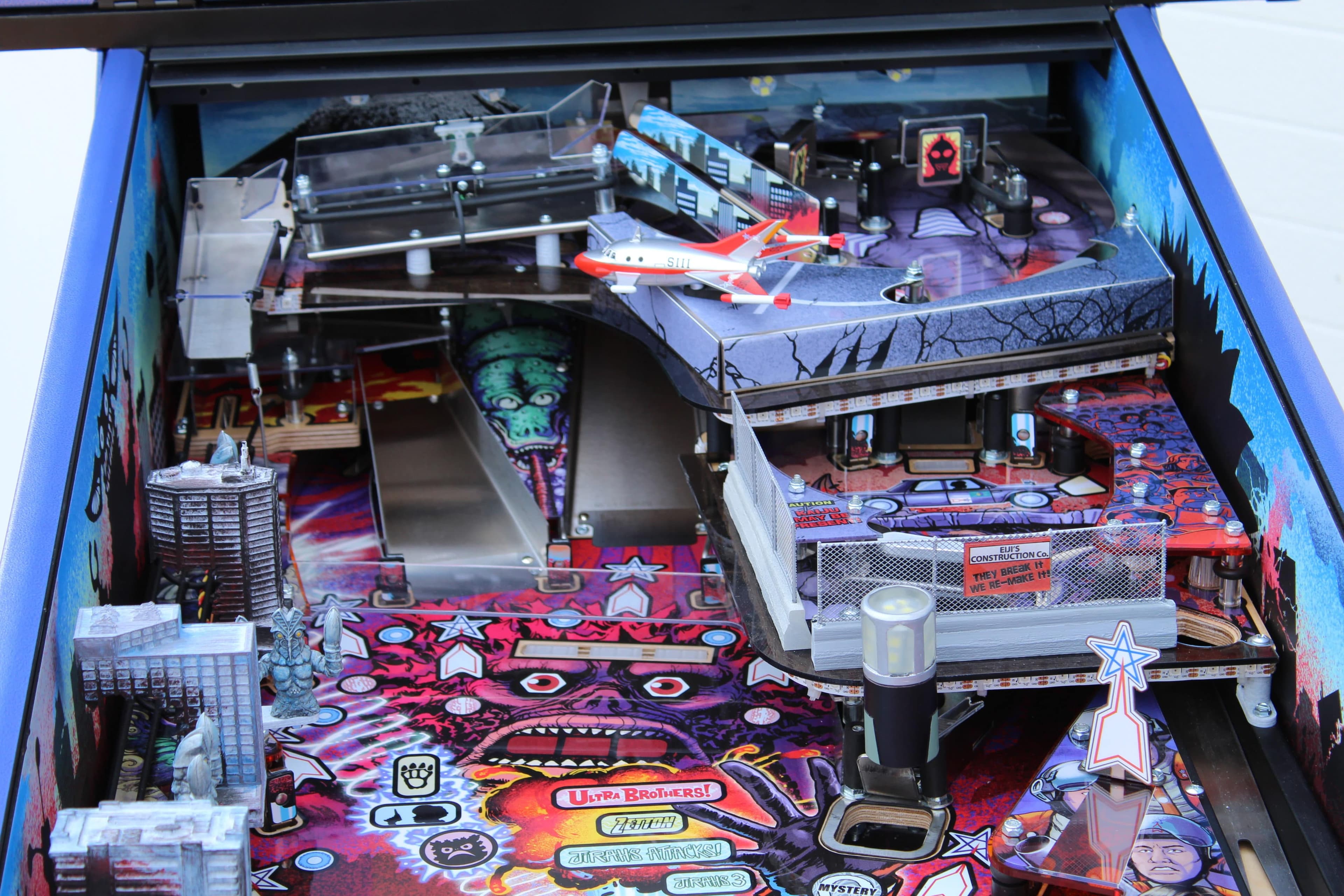 Colorful pinball machine with urban landscape, planes, and monster graphics