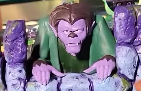 Green-robed purple monster gripping rocky surfaces with intense expression