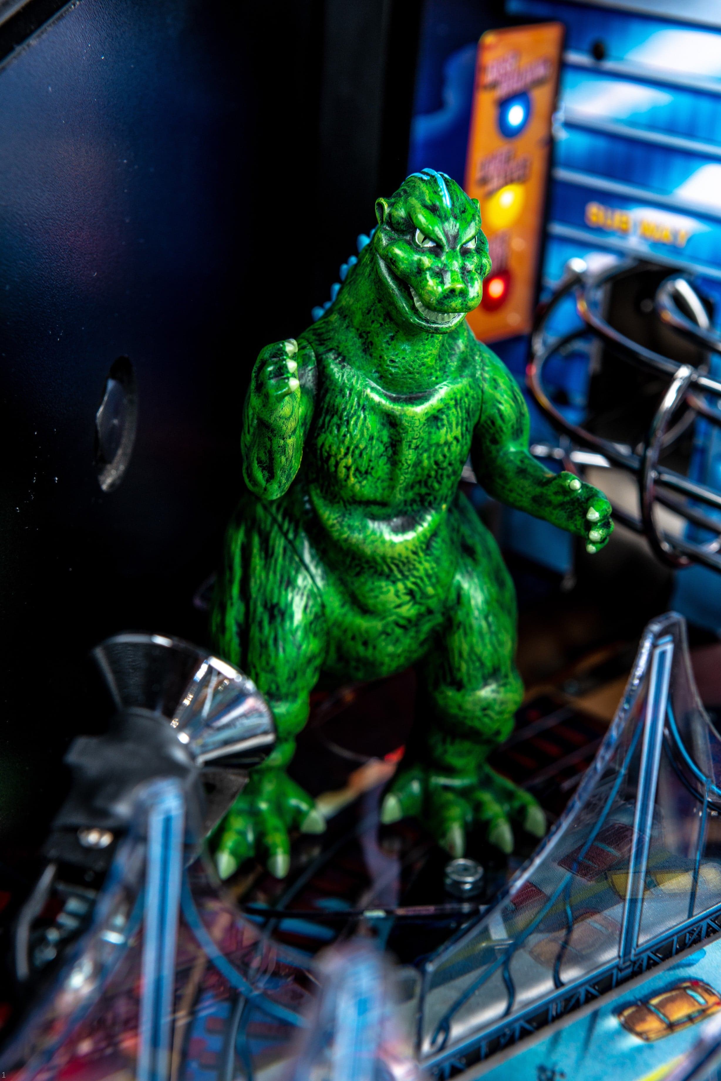 Green Godzilla figurine standing on a cluttered electronic workspace