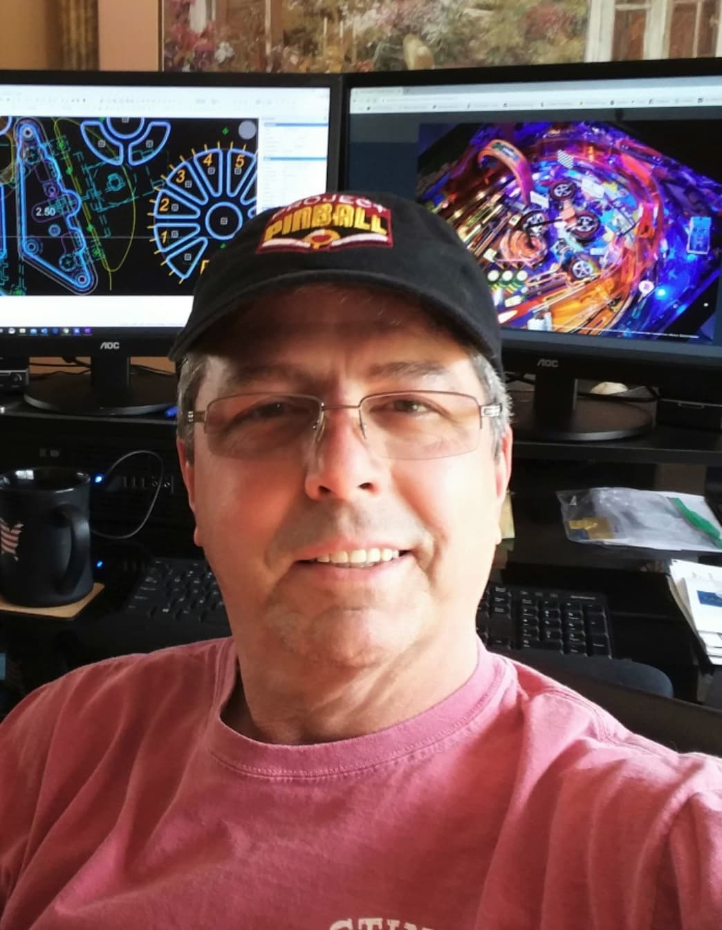 Smiling person wearing pinball hat in front of computer screens showing pinball designs