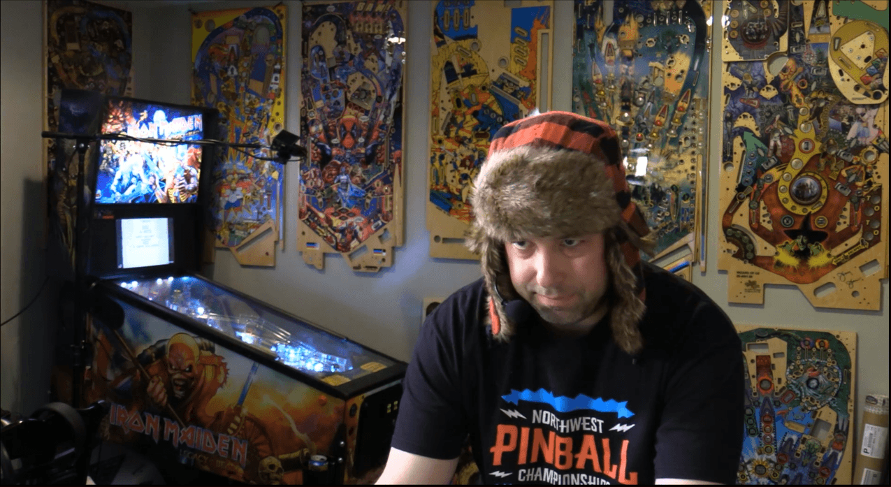 Pinball enthusiast in winter hat surrounded by pinball machines and artwork