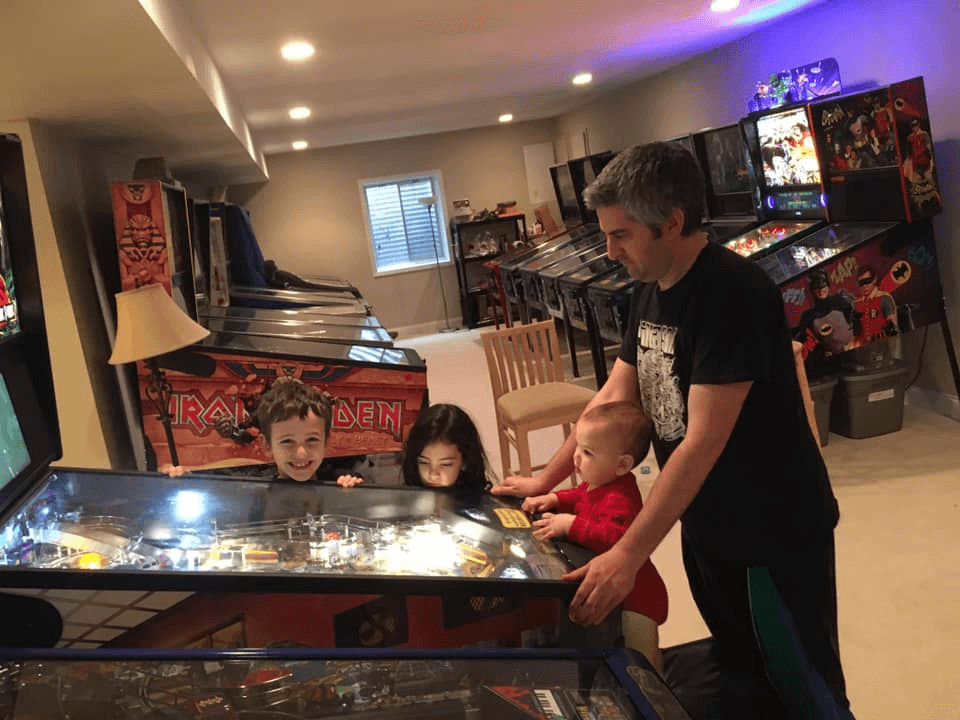 Family playing together on Iron Maiden pinball machine in home game room