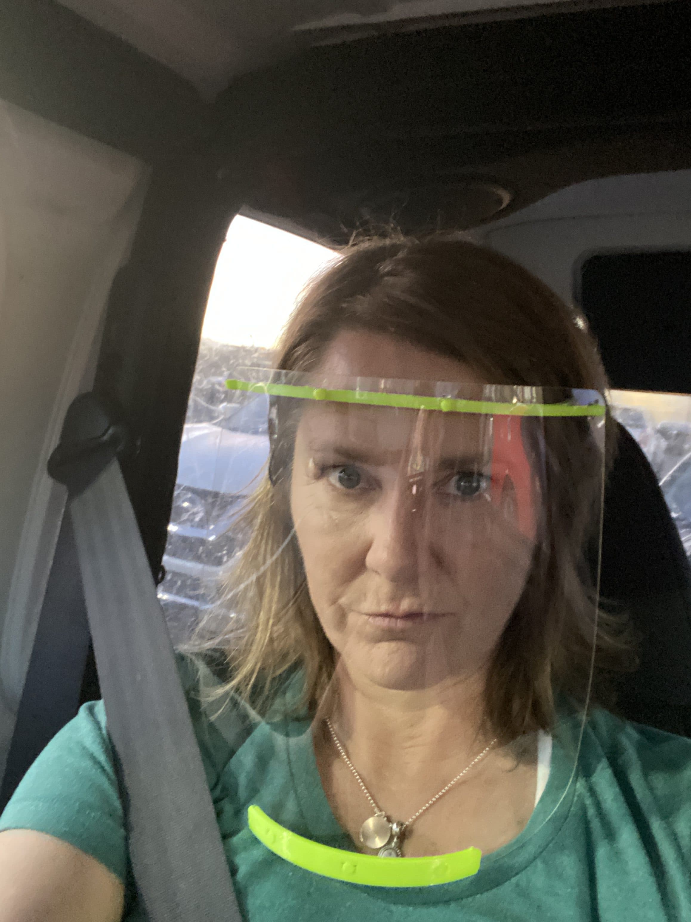 Person wearing green face shield in car, looking serious