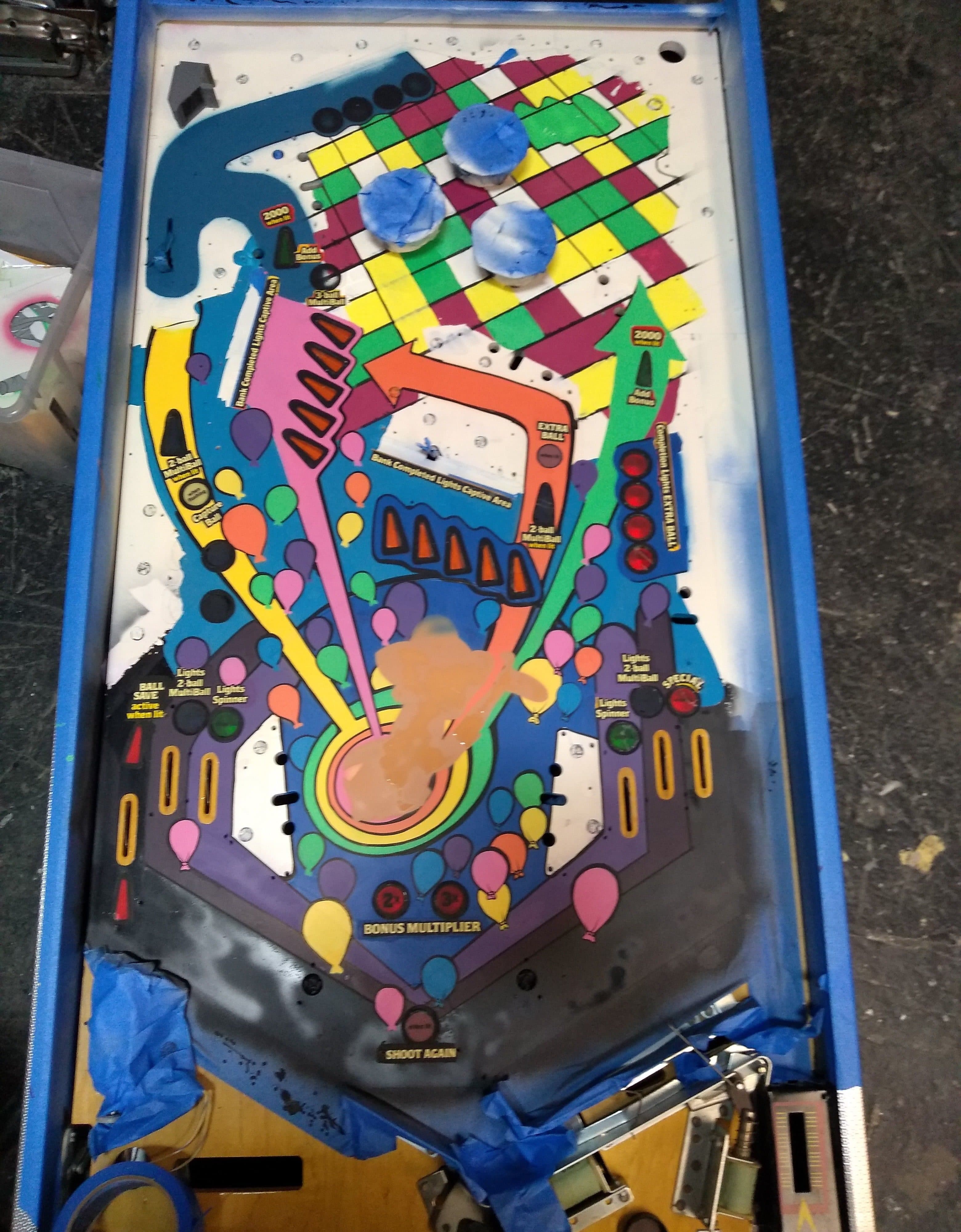 Colorful pinball machine playfield with blue flippers and scattered balloon graphics